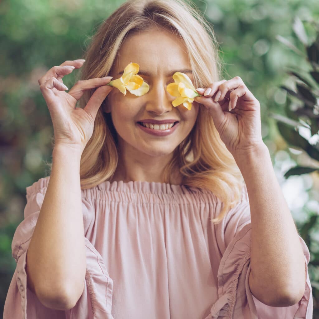 adulte-femme-souriante-posant-des-fleurs-sur-ses-yeux